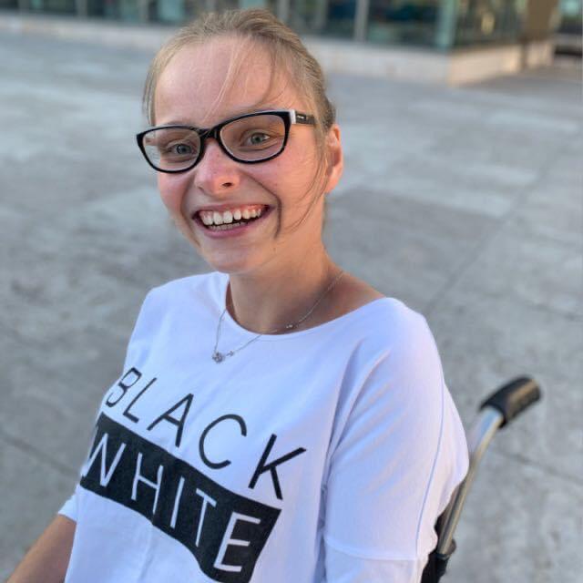 Portrait Anna Mühlhause sitzend im Rollstuhl, au ihrem Tshirt steht black and white